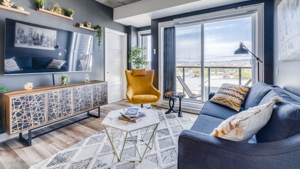 En moderne stue med stort TV, sofa, sofabord og udsigt over byen gennem store vinduer.