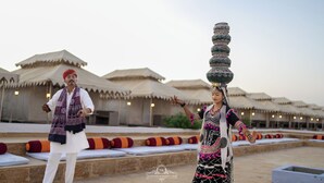 En man och en kvinna, klädda i traditionella dräkter, utför en balansakt med en utsmyckad kruka på huvudet.