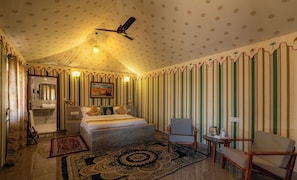 A bedroom with a bed, two chairs, a desk, a mirror, and a bathroom. - NK Desert Camp & Resort (Jaisalmer)