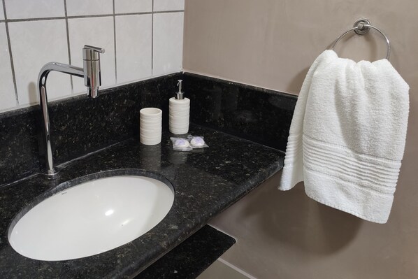 A bathroom with a white sink, black marble countertop, and a towel hanging on a metal ring.