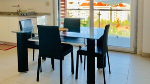 Una cocina moderna con armarios blancos y un comedor con mesa de vidrio y sillas negras.