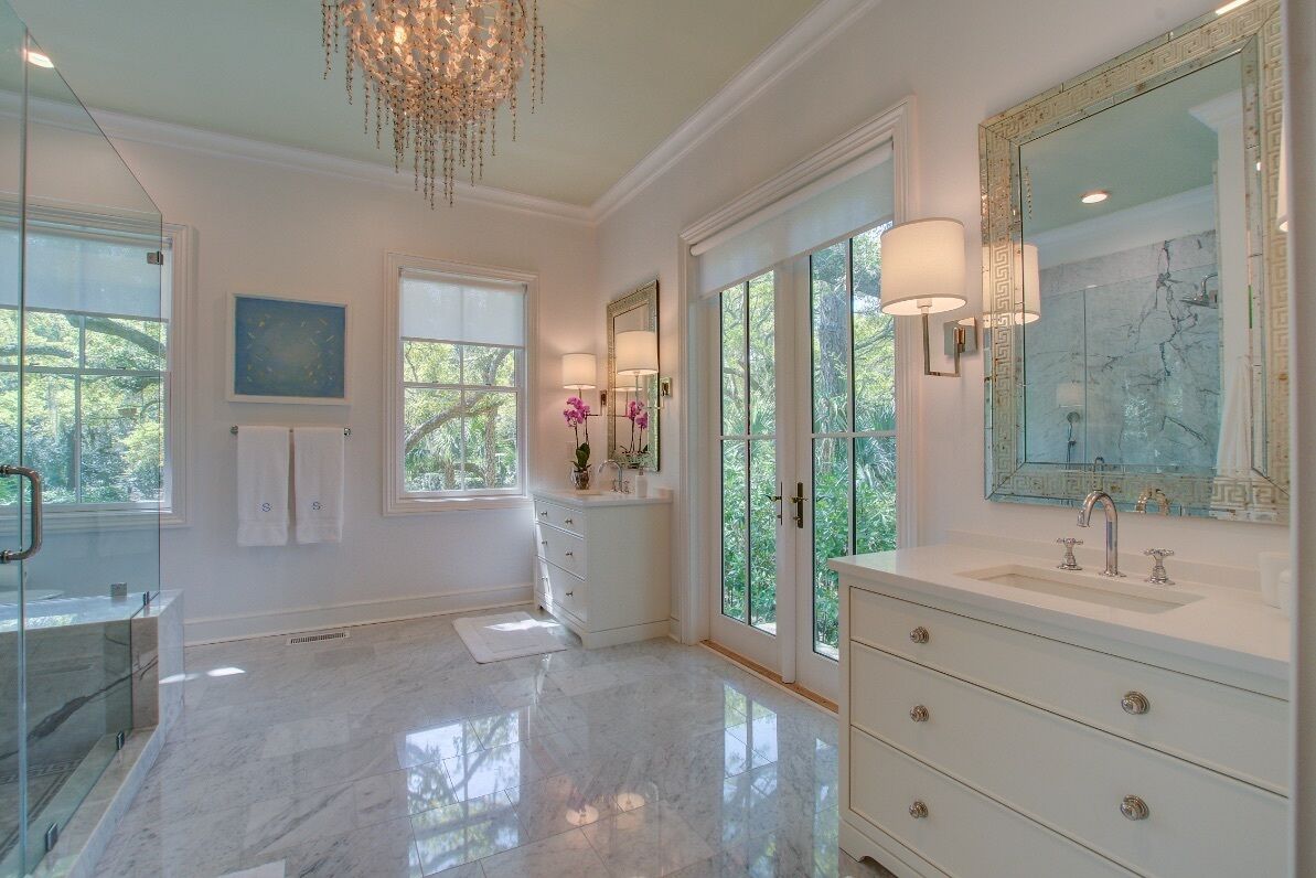 A spacious bathroom with a large mirror, a marble floor, and a glass shower enclosure.