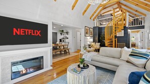 Ein modernes Wohnzimmer mit Kamin, einer Couch, einem Couchtisch und einem Fernseher, der das Netflix-Logo zeigt.