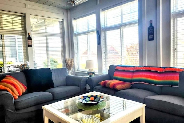 A living room with two grey sofas, a glass coffee table, and a colorful blanket.