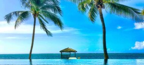 A clear blue sky, a calm sea, and a thatched-roof structure in the water.