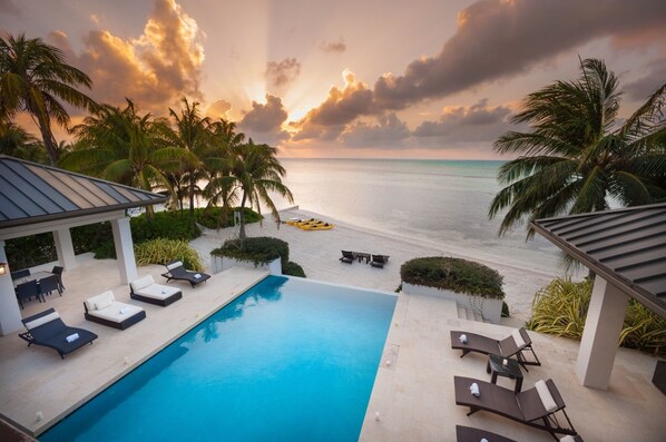A pool area with lounge chairs and a view of the beach and ocean.
