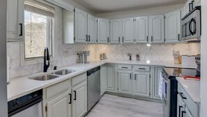 A modern kitchen with white cabinetry, a dishwasher, a microwave, and a sink.