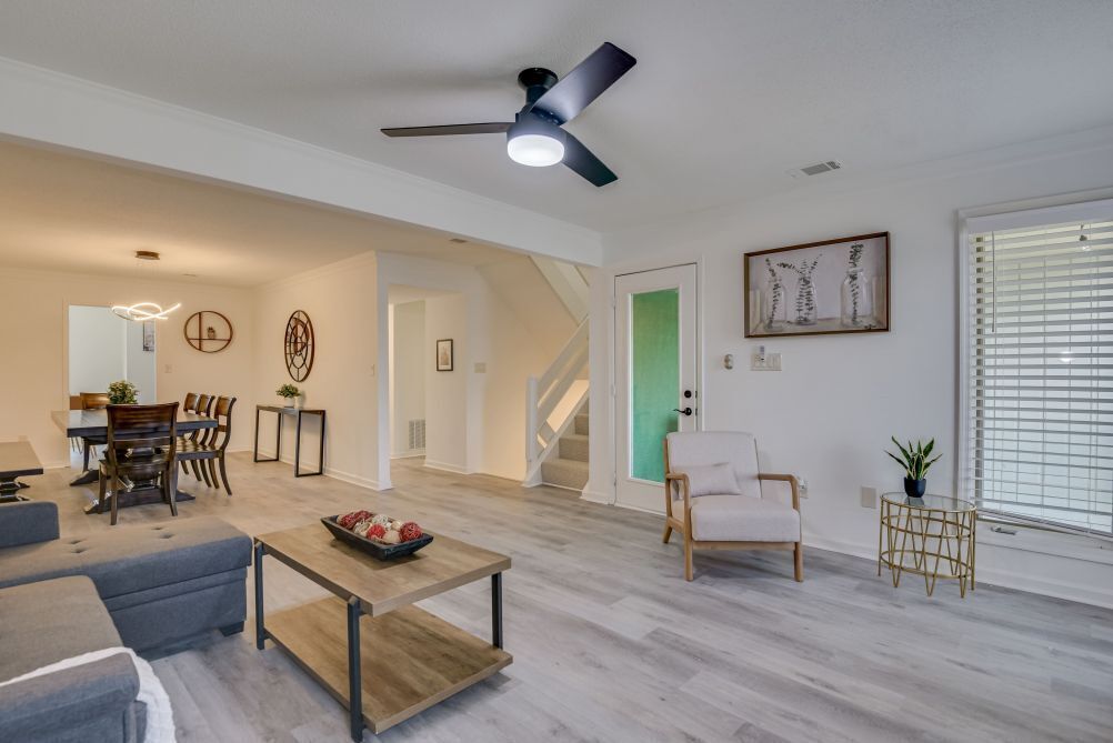 A spacious living room with a dining area, a staircase, and a large window with blinds.
