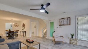 A spacious living room with a dining area, a staircase, and a large window with blinds.