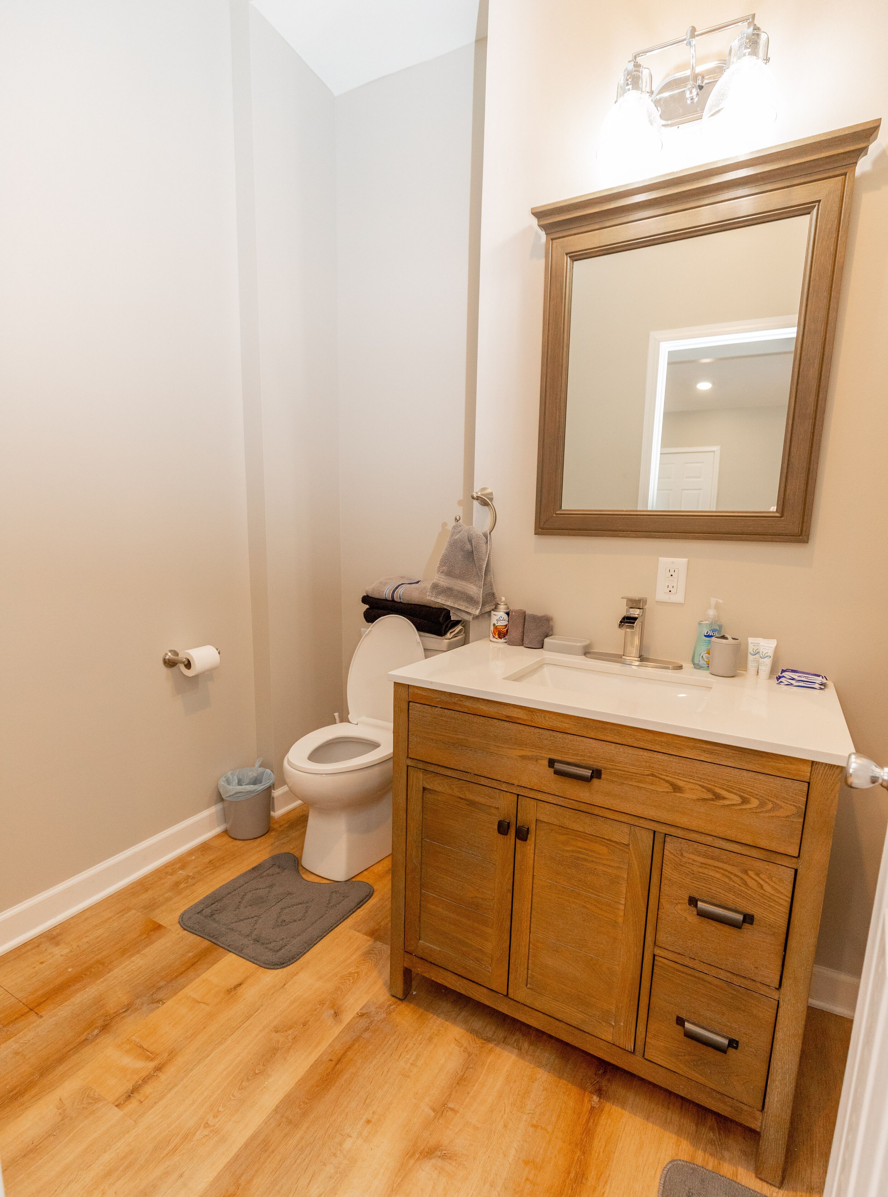 A bathroom with a wooden vanity, a toilet, a mirror, and a small rug on the floor.