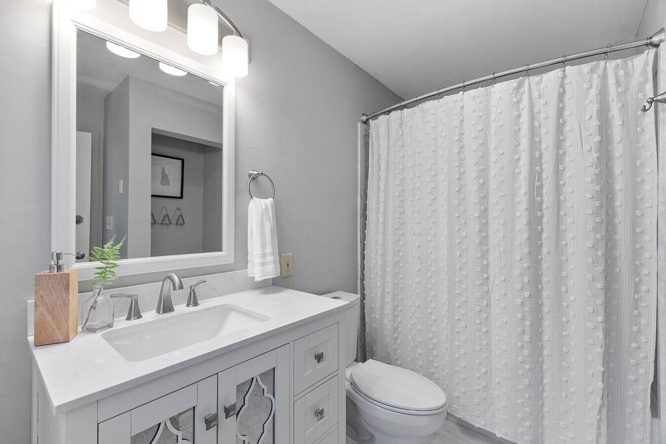 Une salle de bain moderne avec un grand miroir, deux lavabos, des toilettes et un rideau de douche.