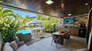 A modern outdoor living area with a pool, dining space, and kitchen. - Flat Luxo Térreo Nannai Residence (Ipojuca)