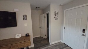 A hallway with a wooden bench, a TV mounted on the wall, and a door with a sign prohibiting smoking and vaping.