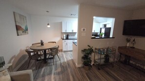 Een moderne keuken met witte kastjes, een eethoek met een ronde tafel en stoelen, en een klein bijzettafeltje met een plant.