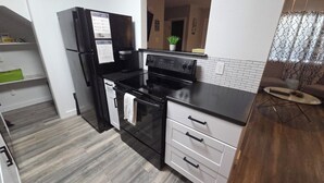 A kitchen with a black refrigerator, a stove, and a sink. There is a plant on the countertop and a towel hanging on the oven handle.