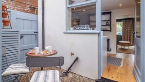 Een klein terras met een tafel gedekt voor twee personen, een stoel en een raam met uitzicht op de keuken.