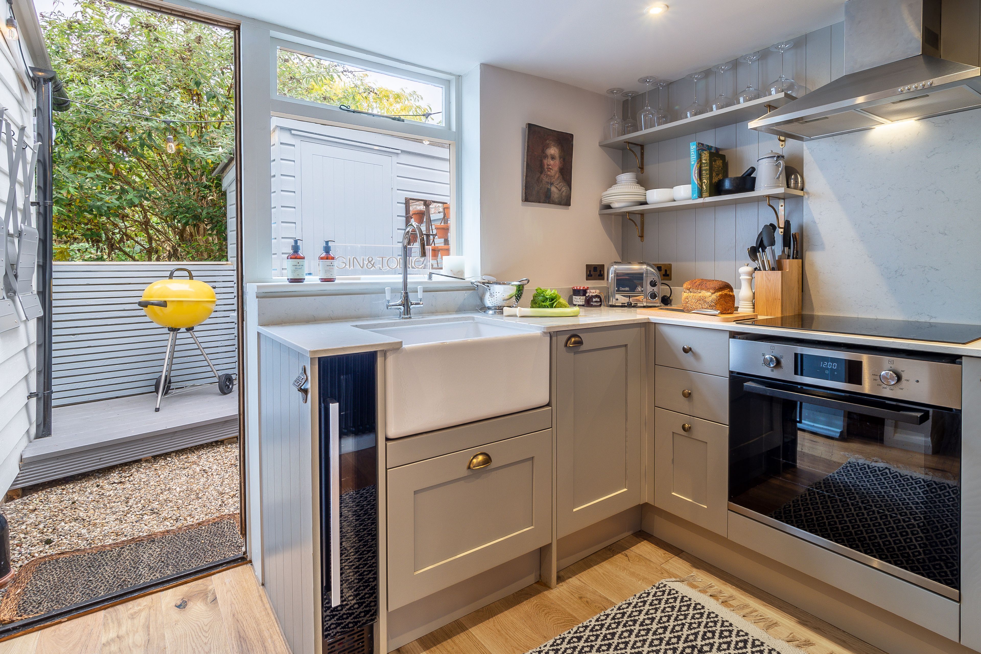 A modern kitchen with a built-in oven, a sink, and a window overlooking a garden.