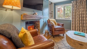Een gezellige woonkamer met een open haard, leren banken, een houten salontafel en een groot raam met gordijnen.