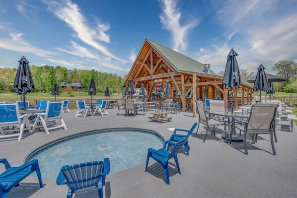 A poolside area with lounge chairs and umbrellas, a wooden structure with a sloped roof, and a clear blue sky.