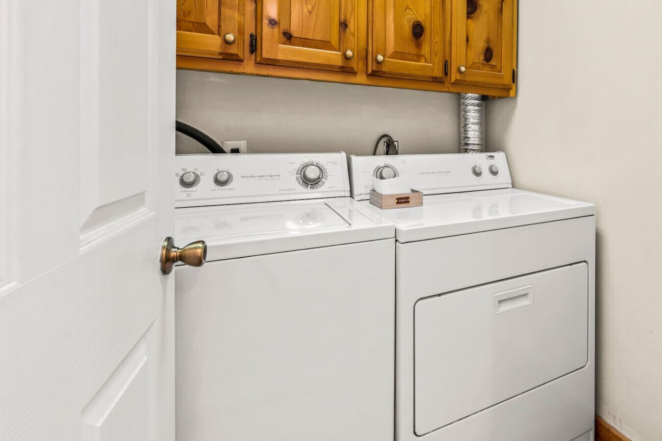 A white washer and dryer unit with wooden cabinets above.
