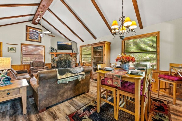 A cozy living room with a fireplace, wooden furniture, and a dining area with a table set for two.