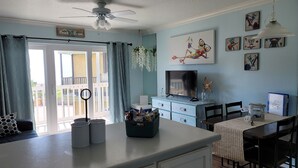 A room with a balcony, a TV, a dining area, and artwork on the walls. - Cute ocean view beach front condo w private balcony . Great LOCATION! Sleeps 6. (Galveston)
