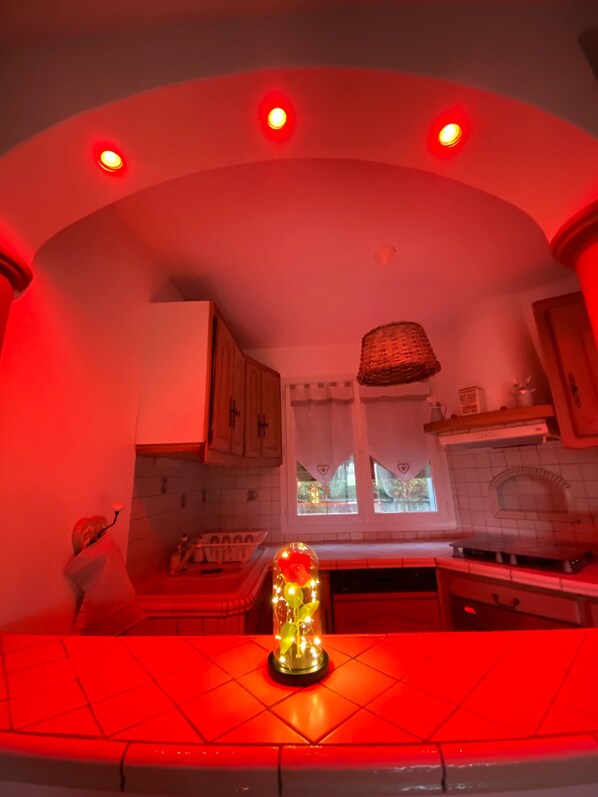 Une cuisine avec un îlot central illuminé de lumière rouge, un dosseret de carreaux blancs et des armoires en bois.