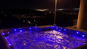 Ein Whirlpool mit blauer Beleuchtung, umgeben von einem Balkon mit Blick auf eine nächtliche Skyline.