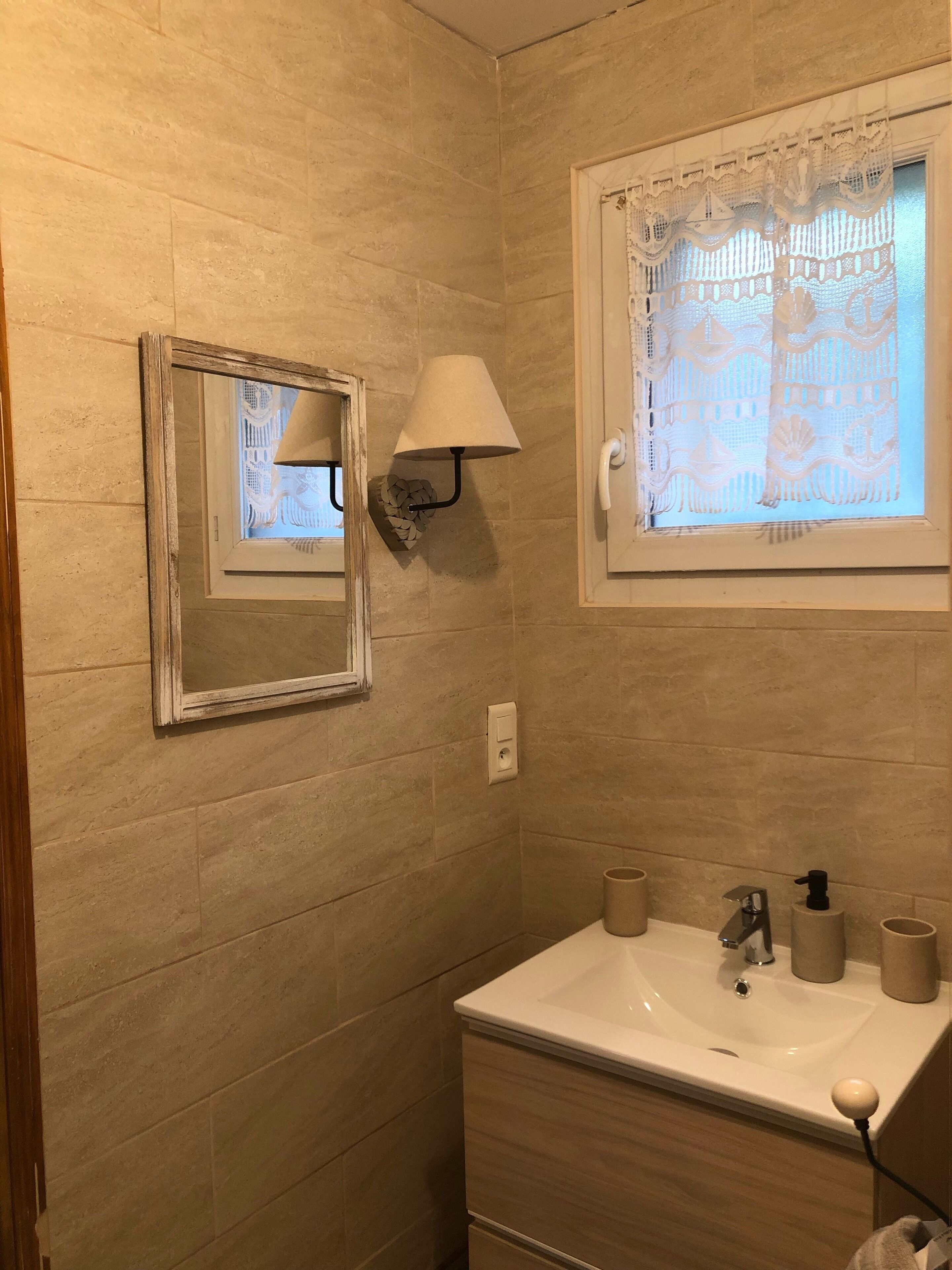 Un baño con lavamanos, espejo y cortinas decorativas.