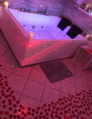 A modern bathroom with a large bathtub, a stone wall, and rose petals on the floor. - Spa house with private Jacuzzi and whirlpool bath overlooking the countryside (Saint-Genest-Lerpt)