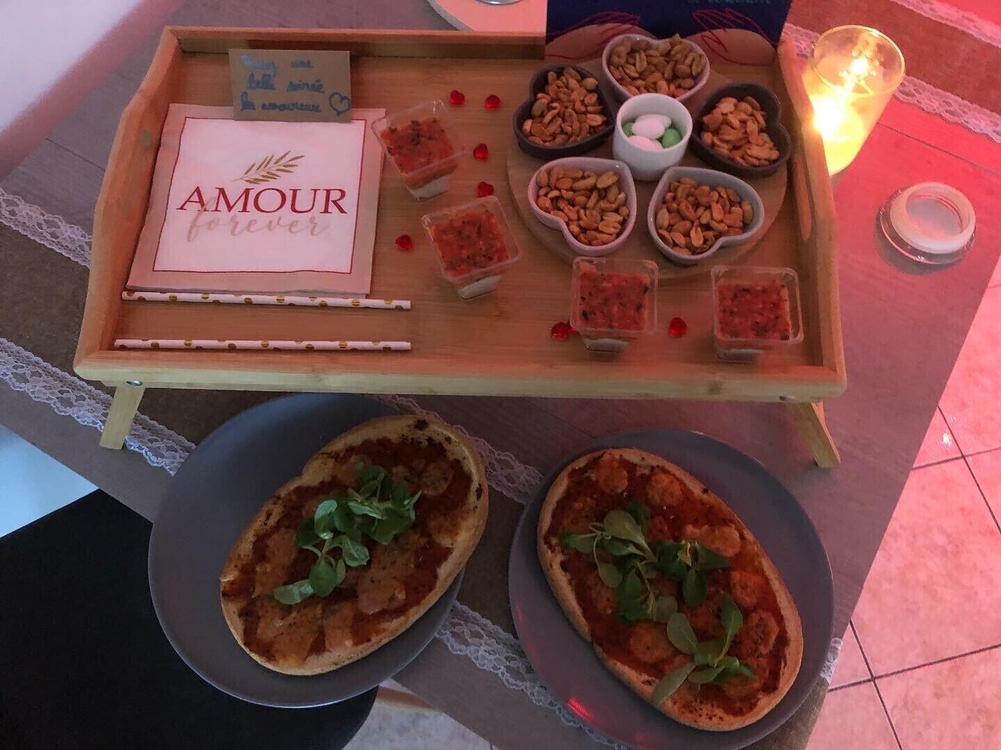 A wooden serving tray with a sign reading "AMOUR forever," containing various food items and two plates of pizza.