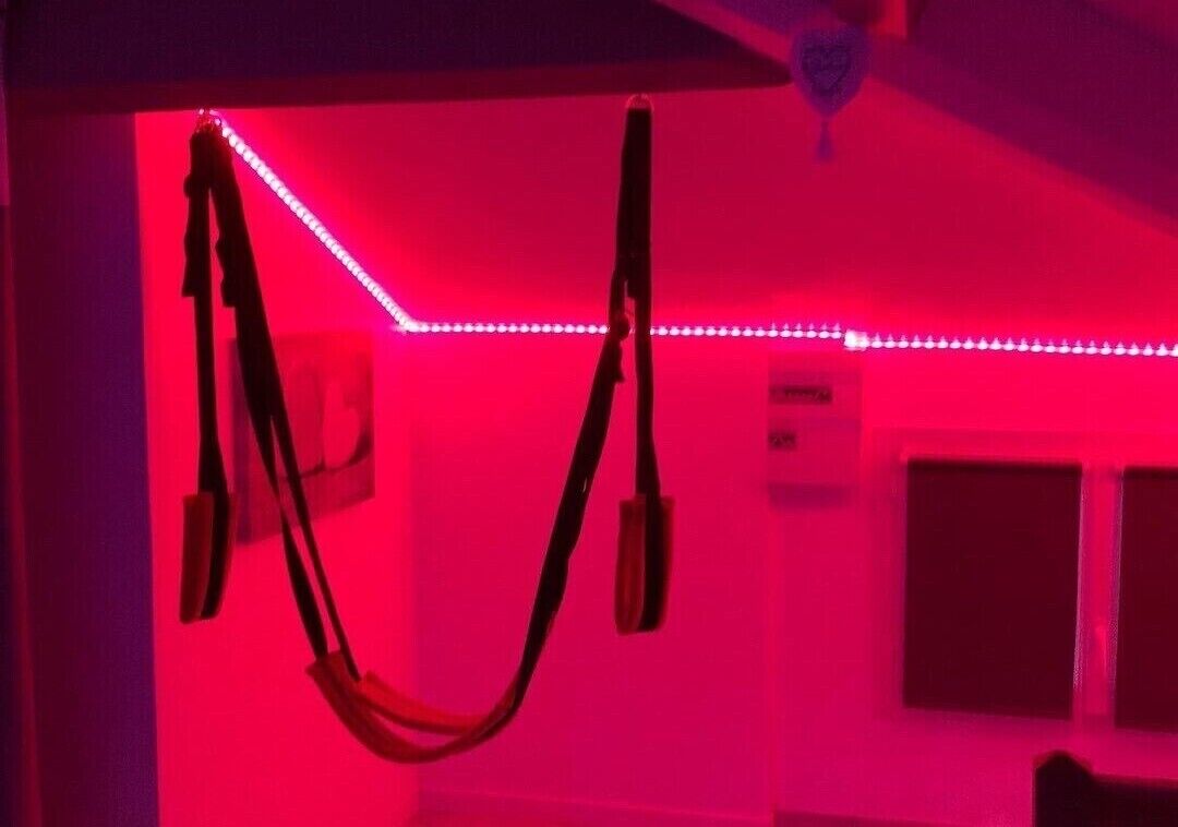 A room with red ambient lighting, a ceiling fan, and a window with blinds.