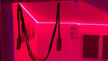 A room with red ambient lighting, a ceiling fan, and a window with blinds.