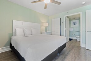 Ein Schlafzimmer mit einem Bett, einem Nachttisch, einem Deckenventilator und einer Tür zu einem Badezimmer.