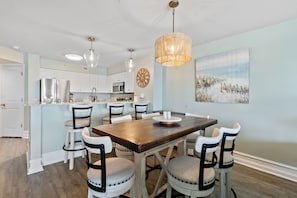 Une cuisine moderne avec des meubles blancs, une table à manger en bois et un luminaire suspendu.