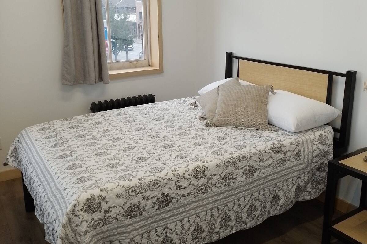 A bedroom with a bed, a window, a radiator, and a chair.