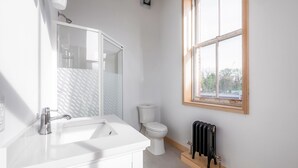 A modern bathroom with a white vanity, a glass shower enclosure, a toilet, and a radiator. - Sandwich Boutique Hotel (Windsor)
