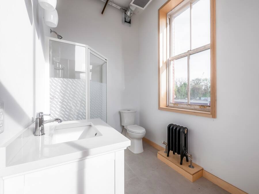 A modern bathroom with a white vanity, a glass shower enclosure, a toilet, and a radiator.