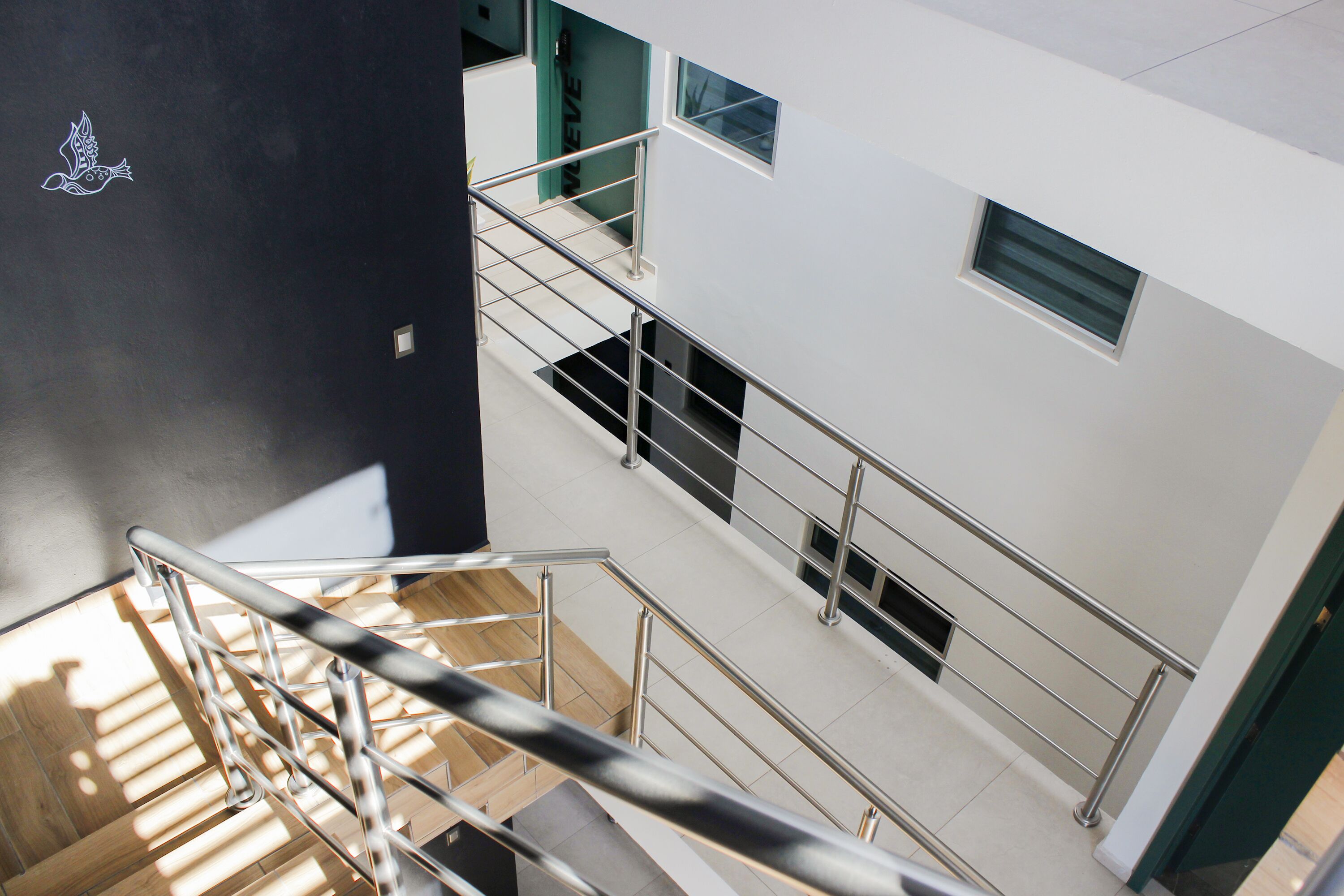 Un intérieur à plusieurs niveaux, avec un escalier, des rampes en métal et une fresque représentant des oiseaux sur le mur.