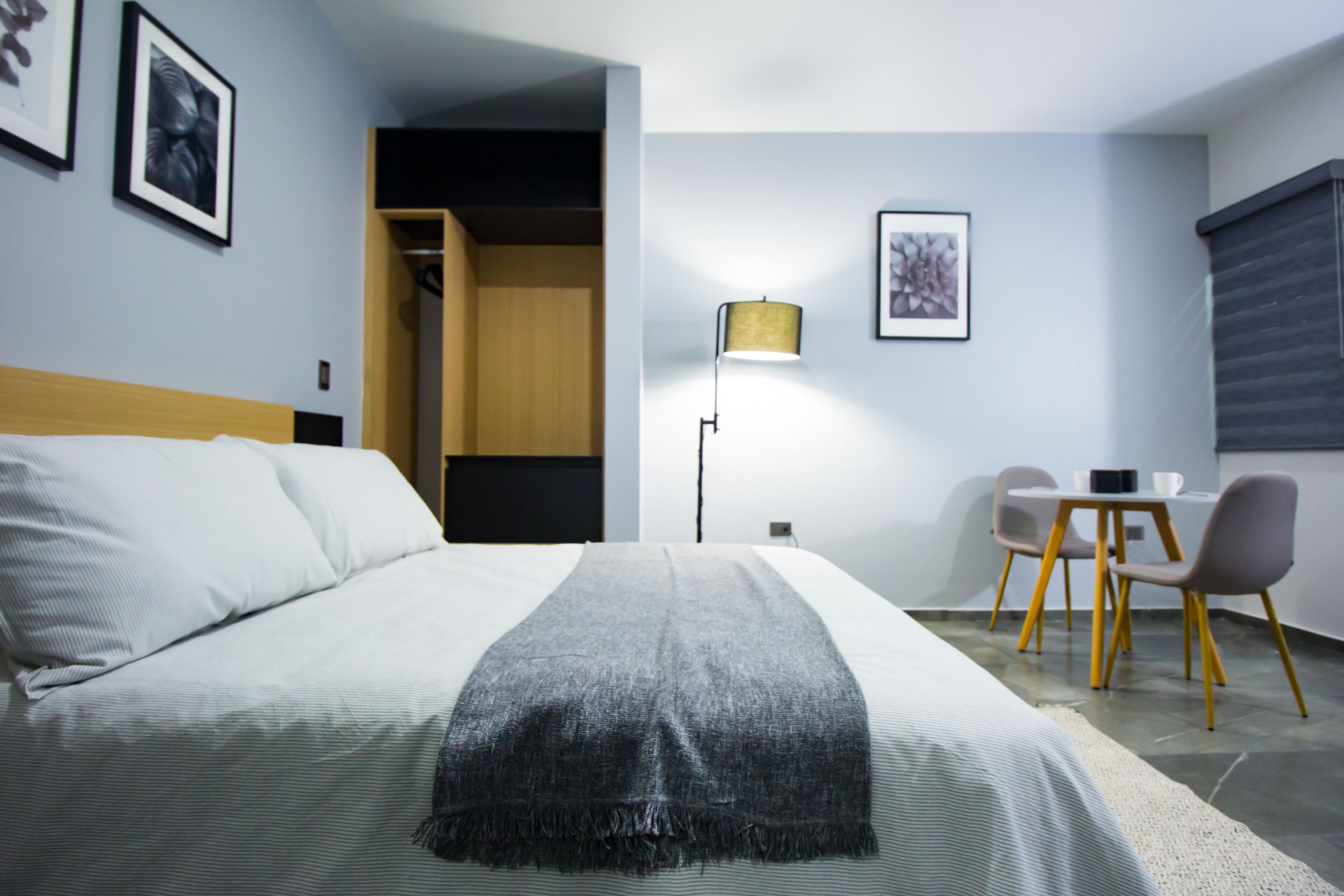 Une chambre d’hôtel avec un lit, un bureau, des chaises, une lampe et des œuvres d’art accrochées aux murs.