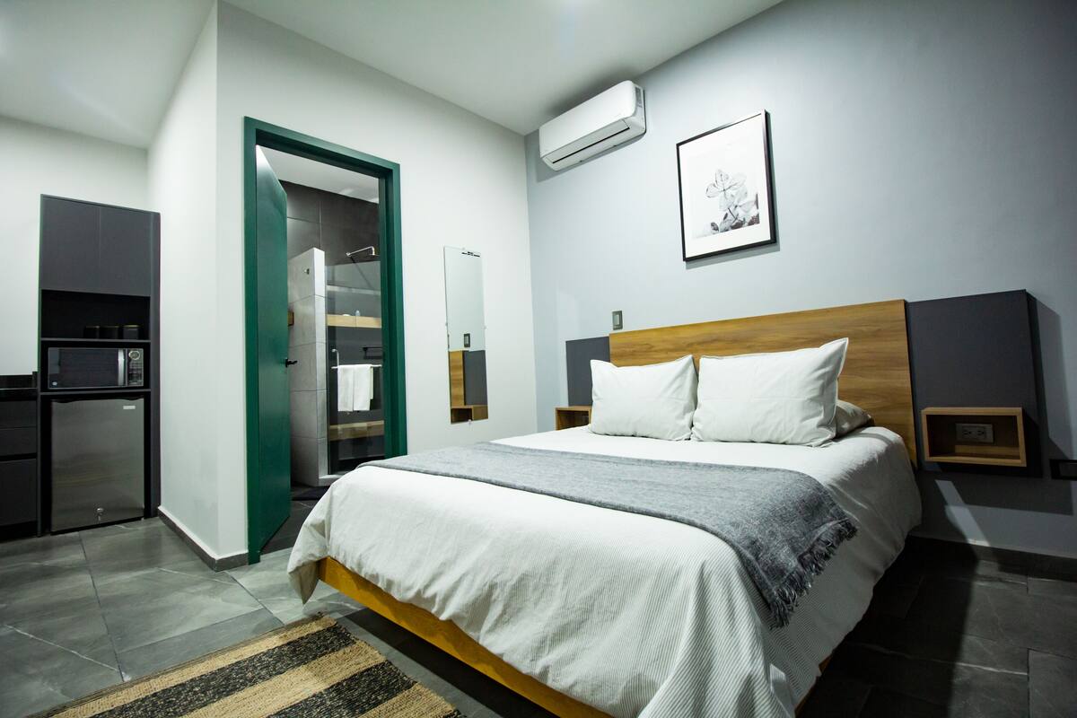 Una habitación de hotel moderna con una cama, un armario, un espejo y un equipo de aire acondicionado.