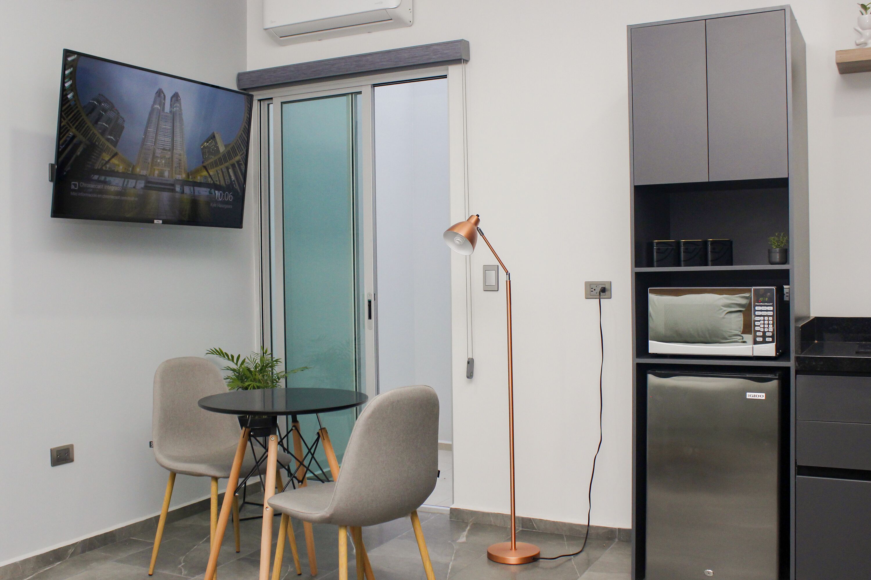 A compact kitchen with a refrigerator, microwave, and a flat-screen TV mounted on the wall.