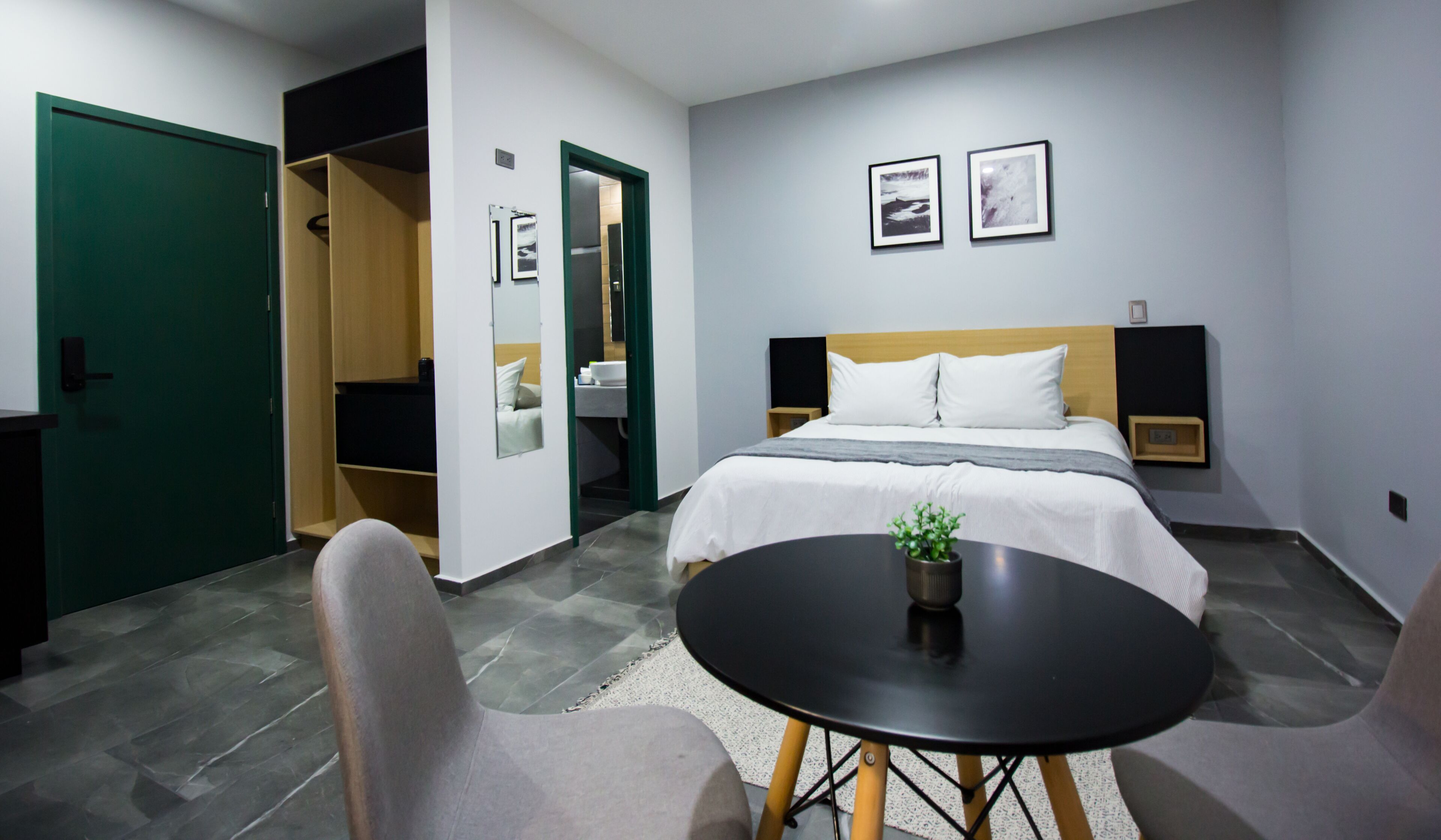 Quarto de hotel com uma cama, mesas de cabeceira, uma pequena mesa com uma planta e uma porta verde.