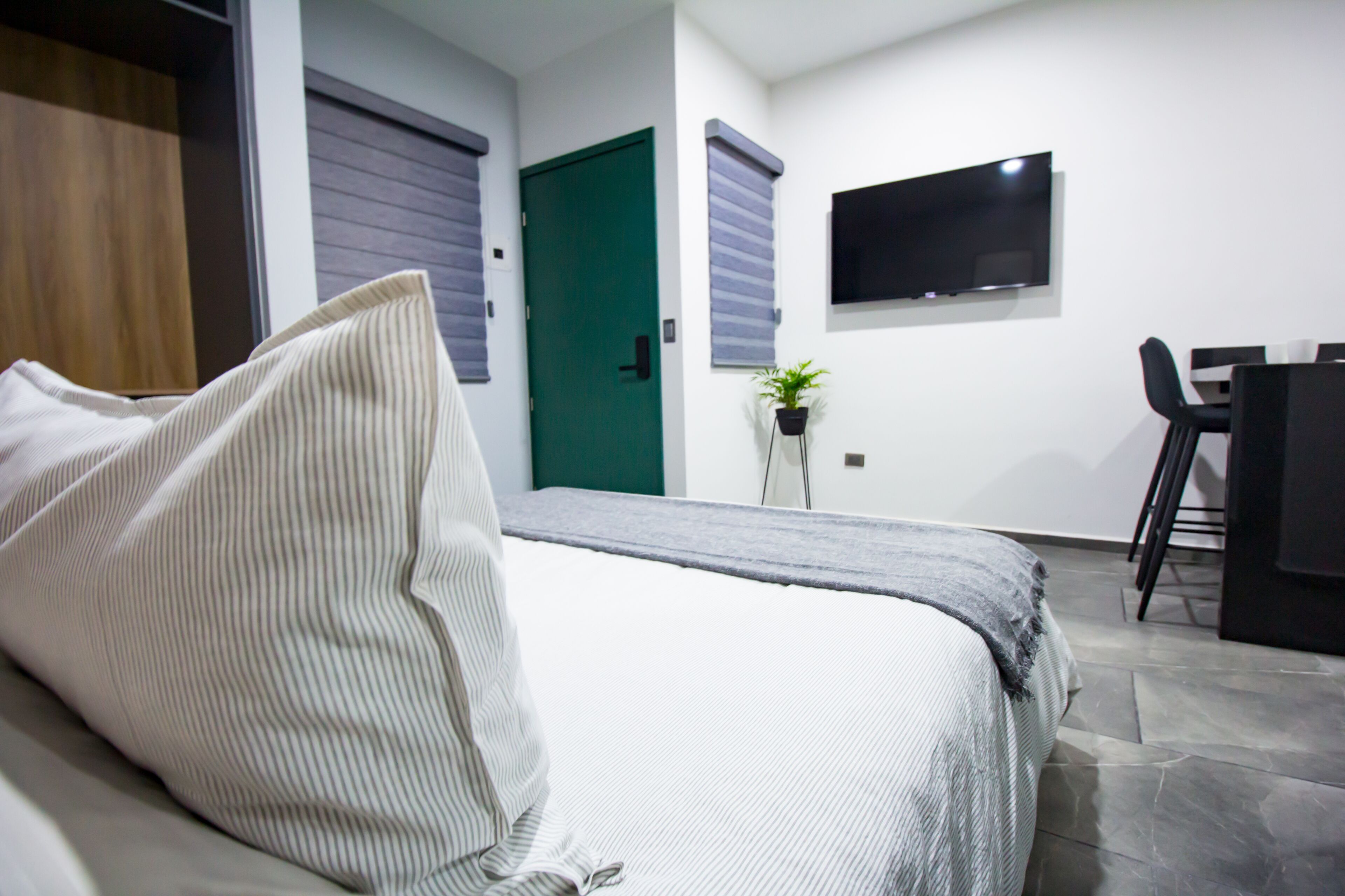 A modern hotel room with a bed, a desk, a chair, a TV, and a green door.