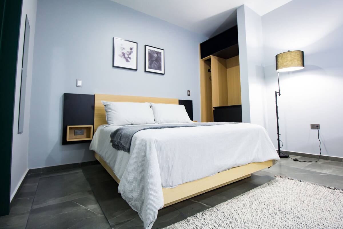 Un dormitorio moderno con una cama, una mesita de noche, una lámpara y dos cuadros en la pared.