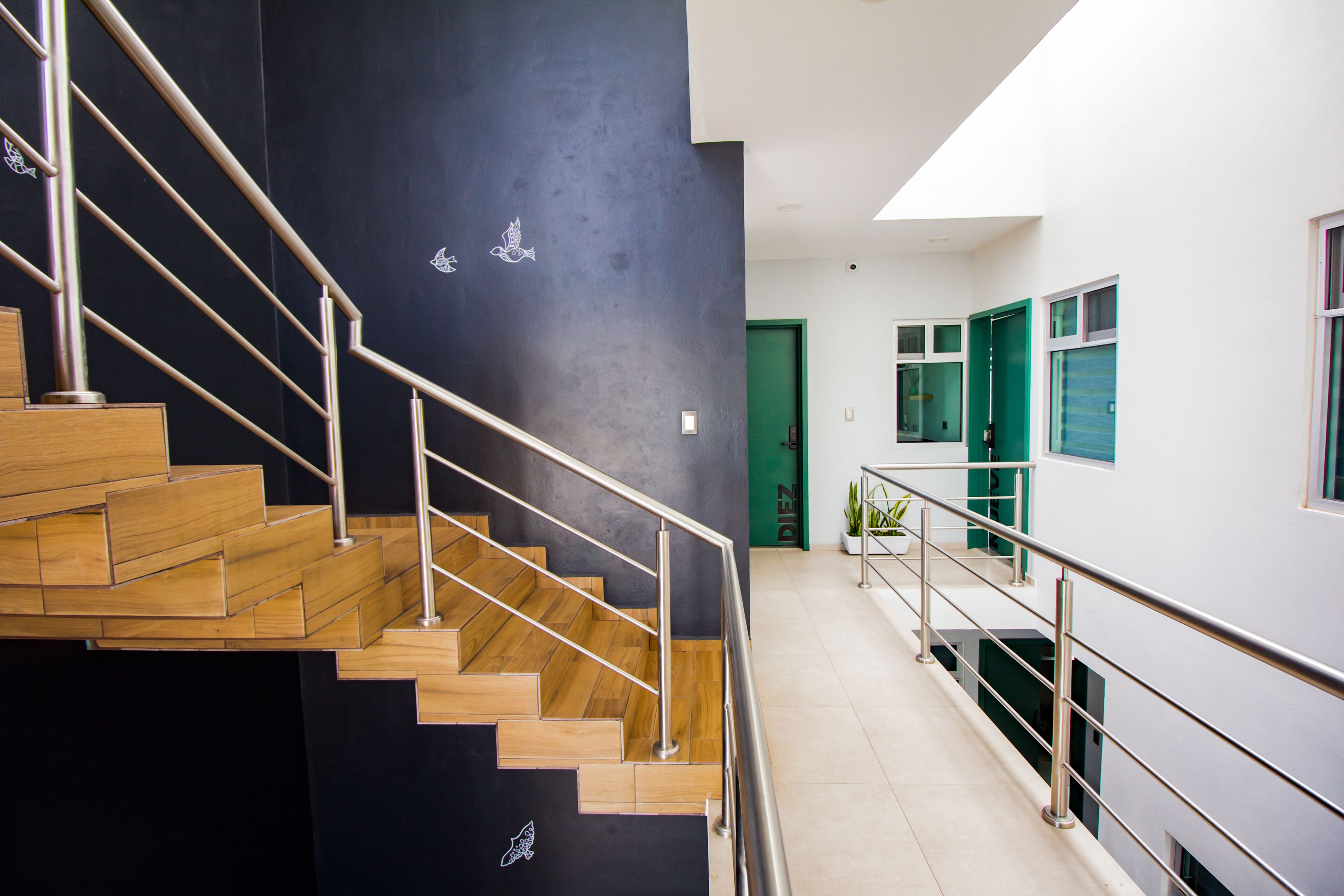 Un intérieur moderne avec un escalier en bois et des rampes en métal, une porte verte et un mur blanc avec une fenêtre.
