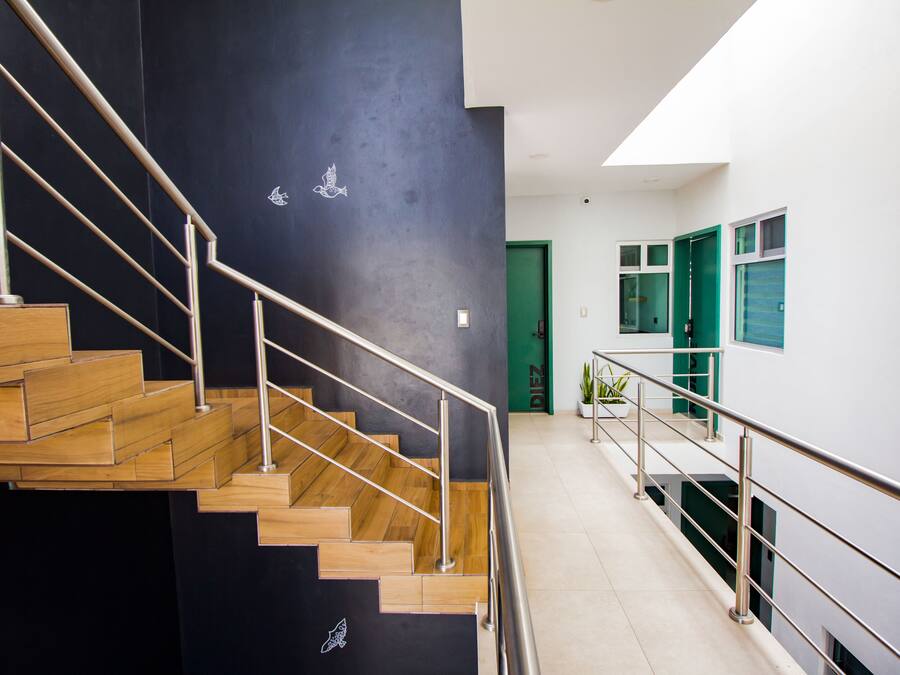 Un intérieur moderne avec un escalier en bois et des rampes en métal, une porte verte et un mur blanc avec une fenêtre.