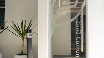 A modern building entrance with a glass door, a potted plant, and a vertical sign with text.