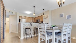 A kitchen with wooden cabinets, a central island, and a dining area with white chairs. - Lake & Golf View 3 bedroom Condo 1516 with Resort access and short walk to beach (North Myrtle Beach)
