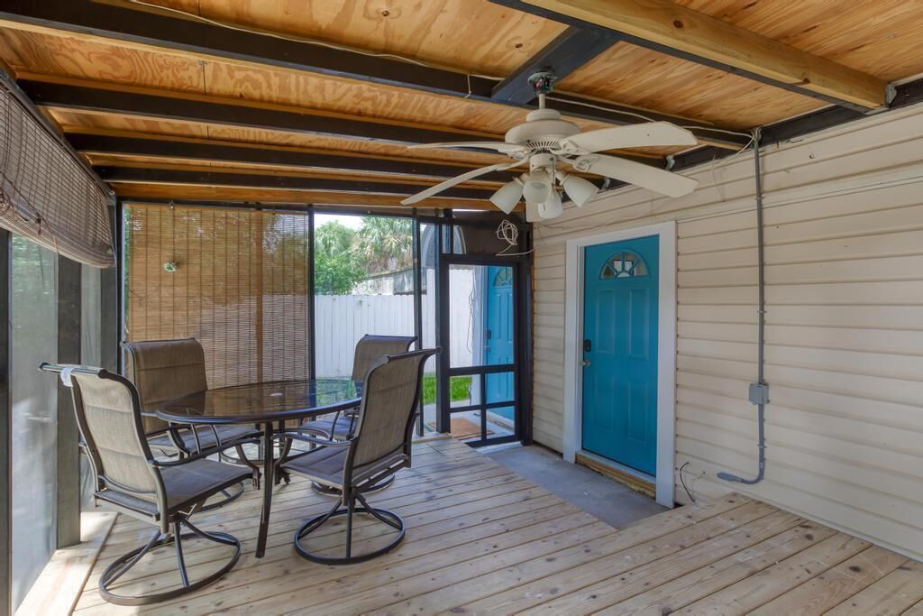 An outdoor patio with a round table and four chairs, a ceiling fan, and a blue door.